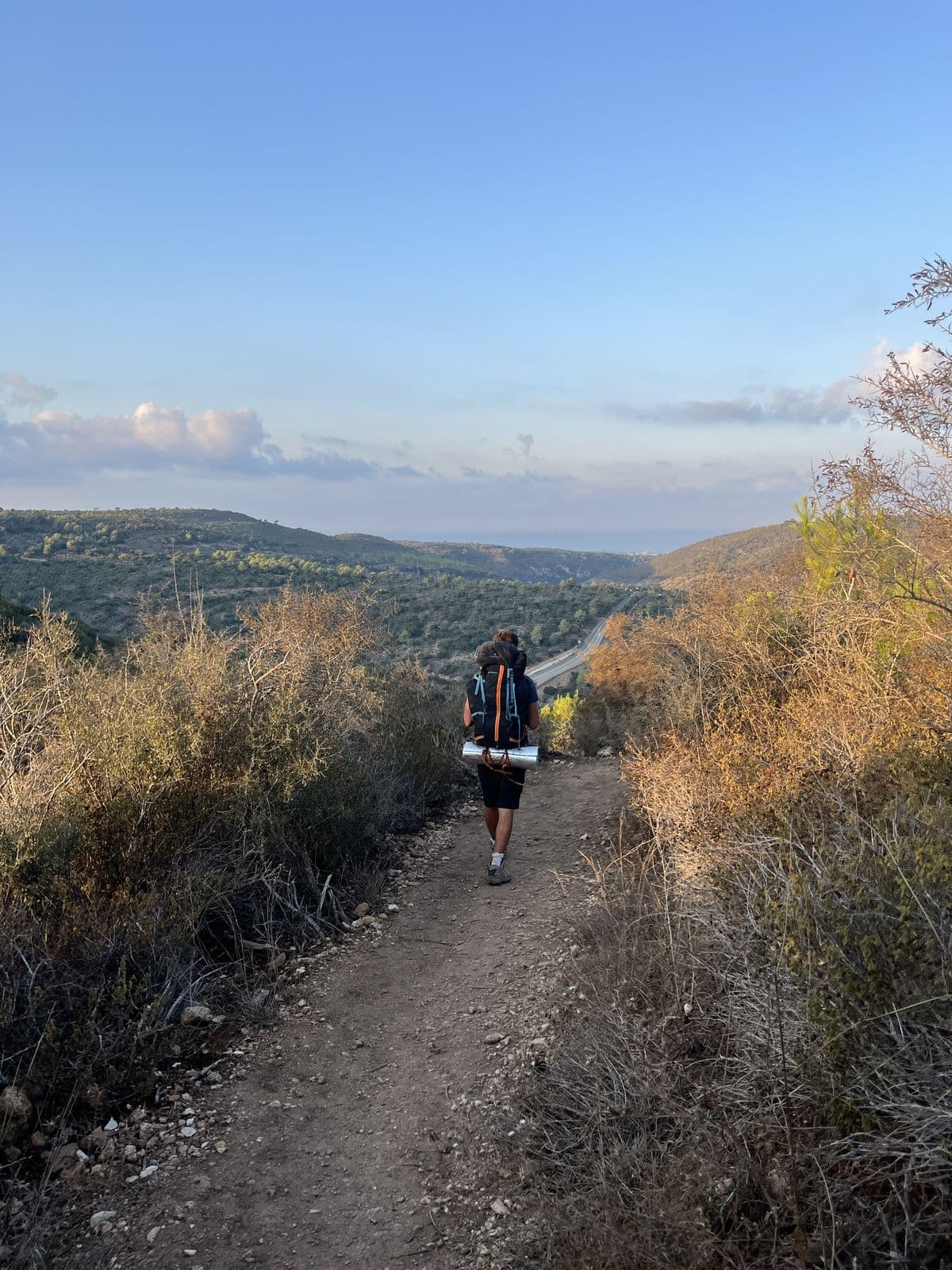 משתתף עם תרמיל ומזרן הולך בשביל עפר בגליל, בשעת אור אחרונה