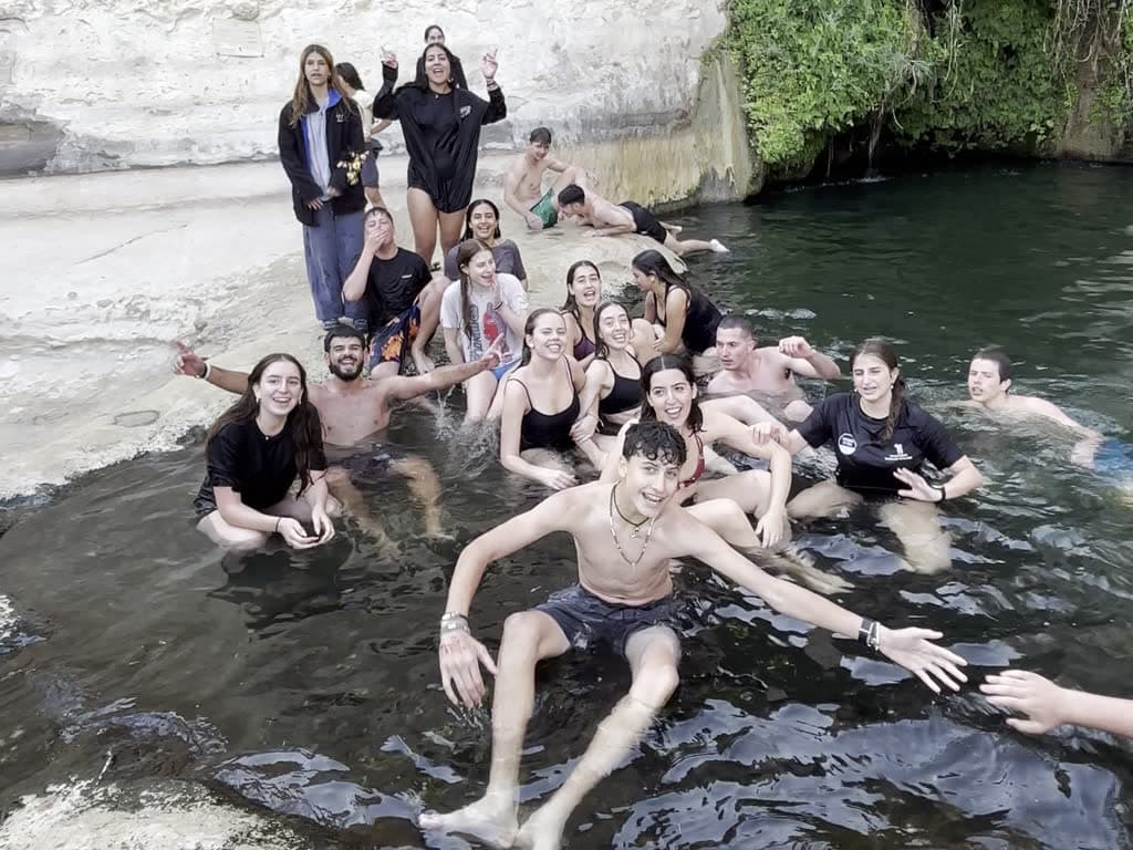 The whole group together at a spring at the end of a journey day, waving at the camera
