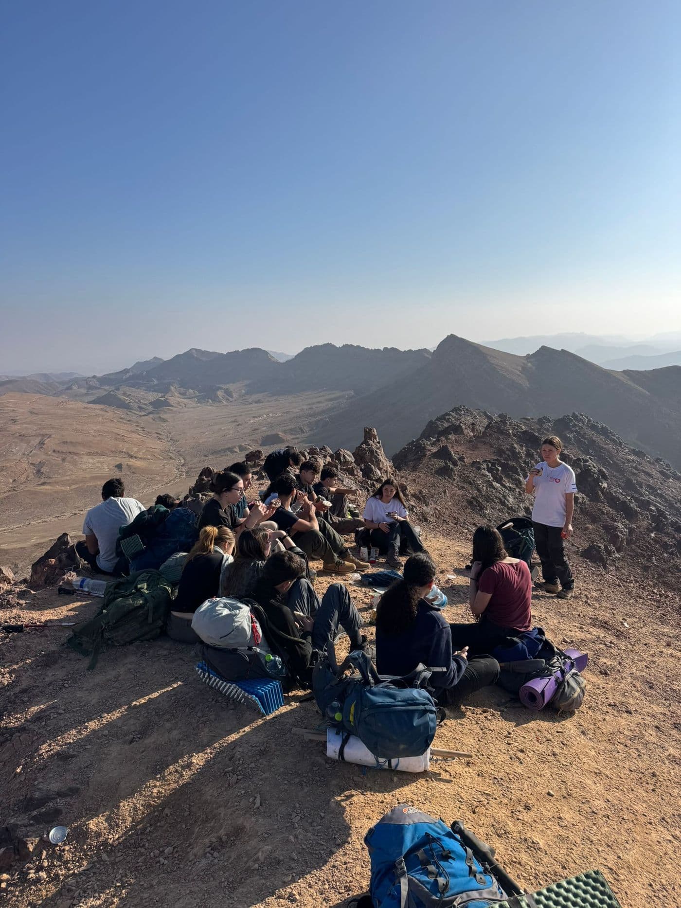 The group sitting together on a summit facing a mountain view