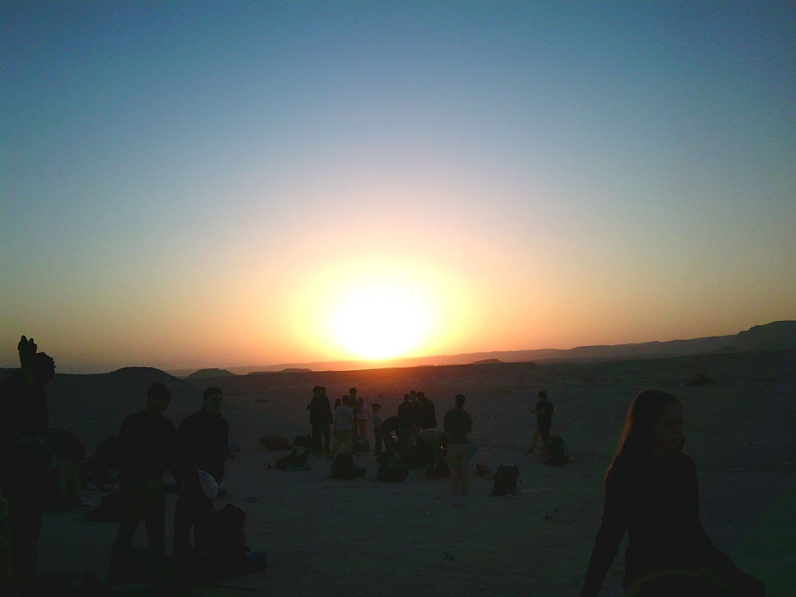 Silhouettes of participants on a ridge against a desert sunset